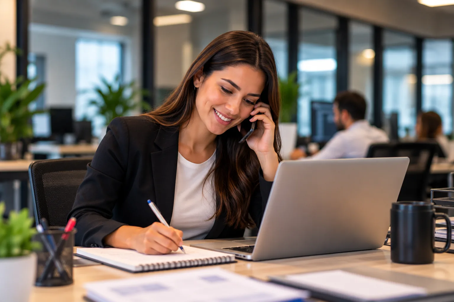 Pessoa do atendimento ao telefone com um cliente, anotando ao lado do notebook.